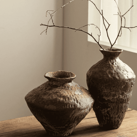 Two rustic ceramic vases on a wooden surface with a neutral background