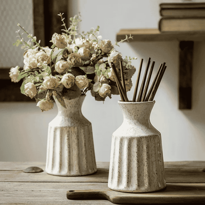 Two ceramic vases with a bouquet of flowers and reed diffuser on a wooden surface.