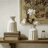 Decorative setting with a textured vase, stack of books, and a small jar on a shelf.