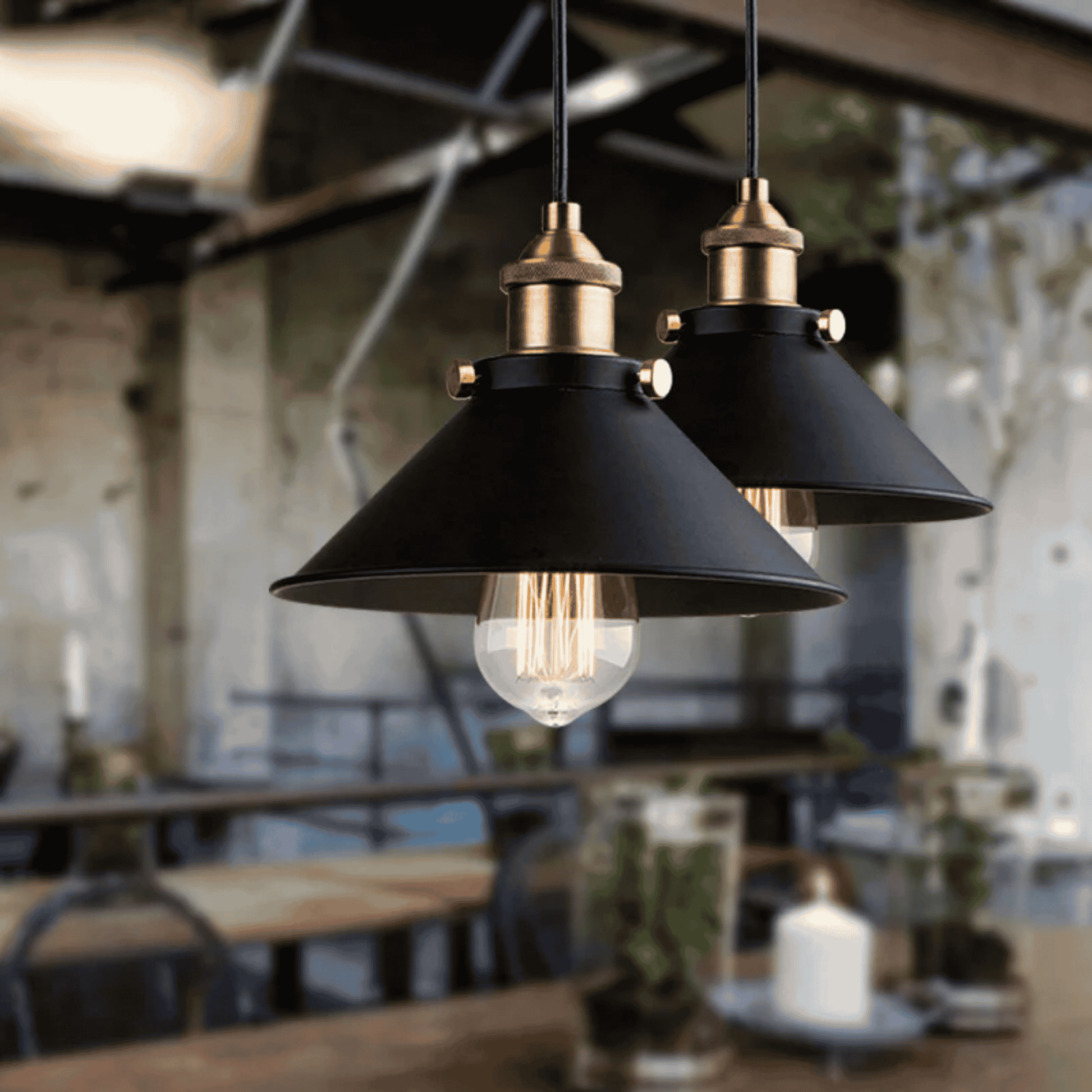 Two black pendant lights with gold accents hanging in a blurred indoor setting.