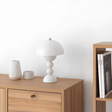 Wooden sideboard with a white lamp and decorative items against a white wall.