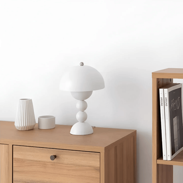 Wooden sideboard with a white lamp and decorative items against a white wall.