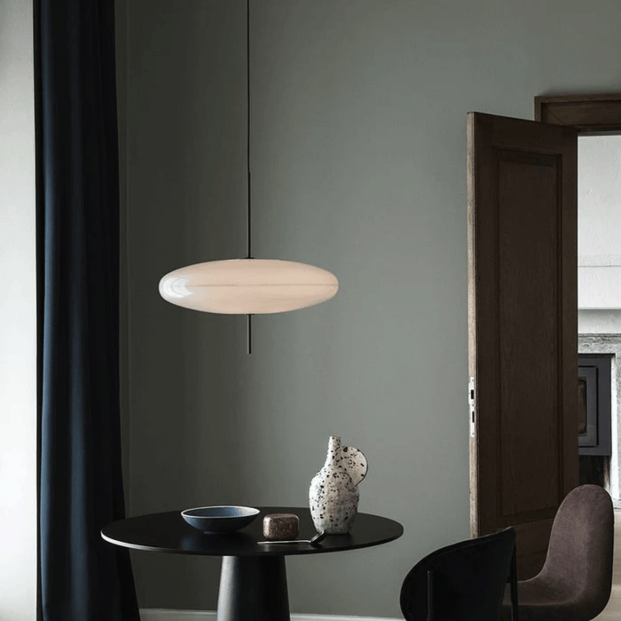 Modern pendant light hanging above a table with decorative items against a gray wall.