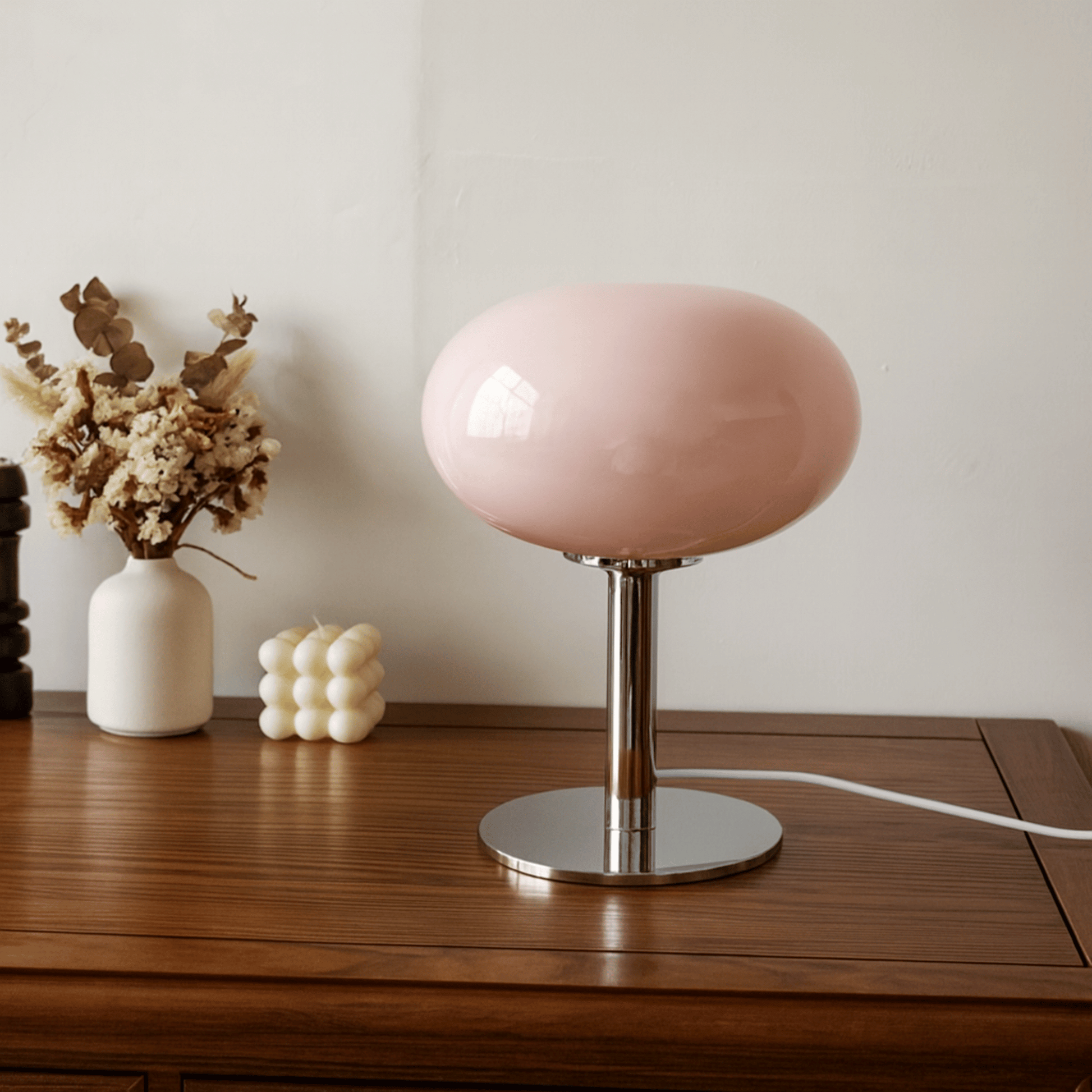 Pink table lamp on a wooden surface with decorative items in the background