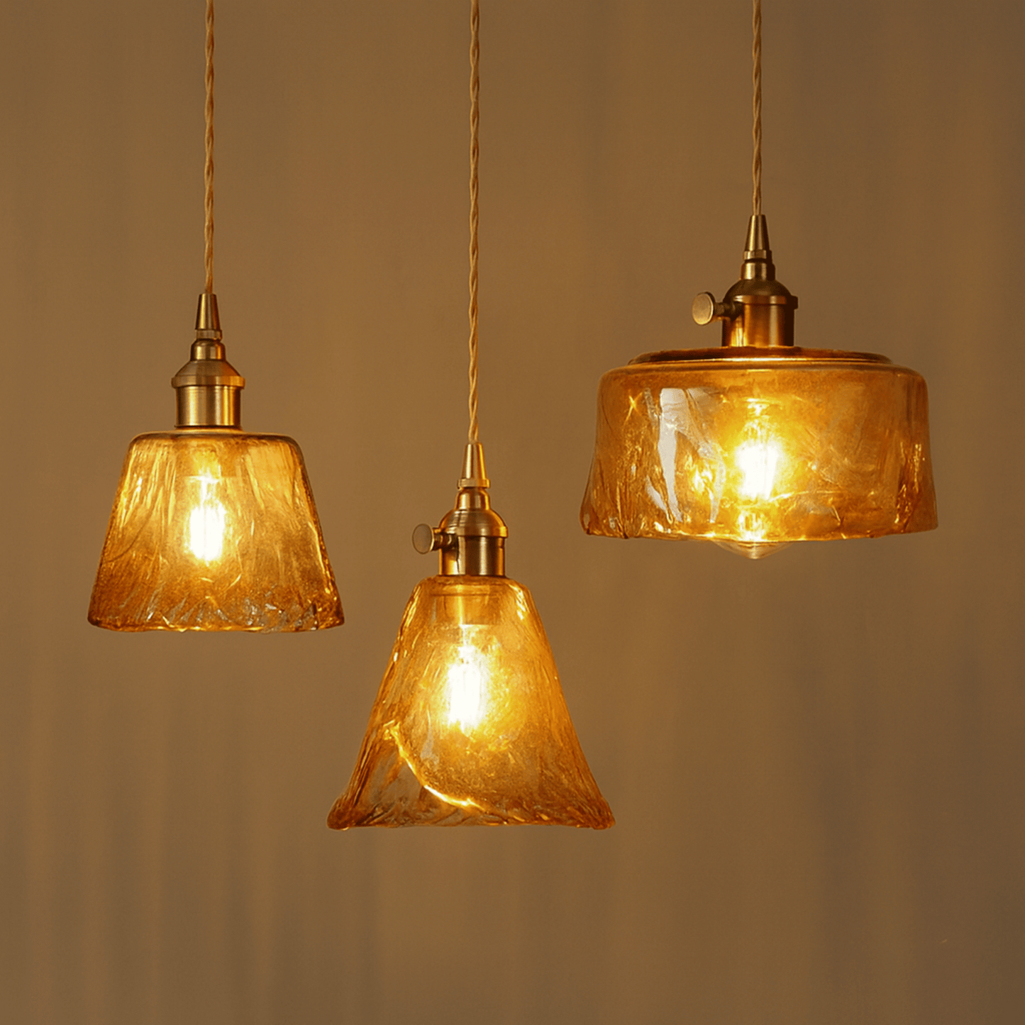 Three amber glass pendant lights with gold fixtures on a neutral background