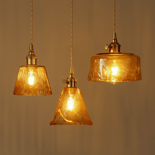 Three amber glass pendant lights with gold fixtures on a neutral background