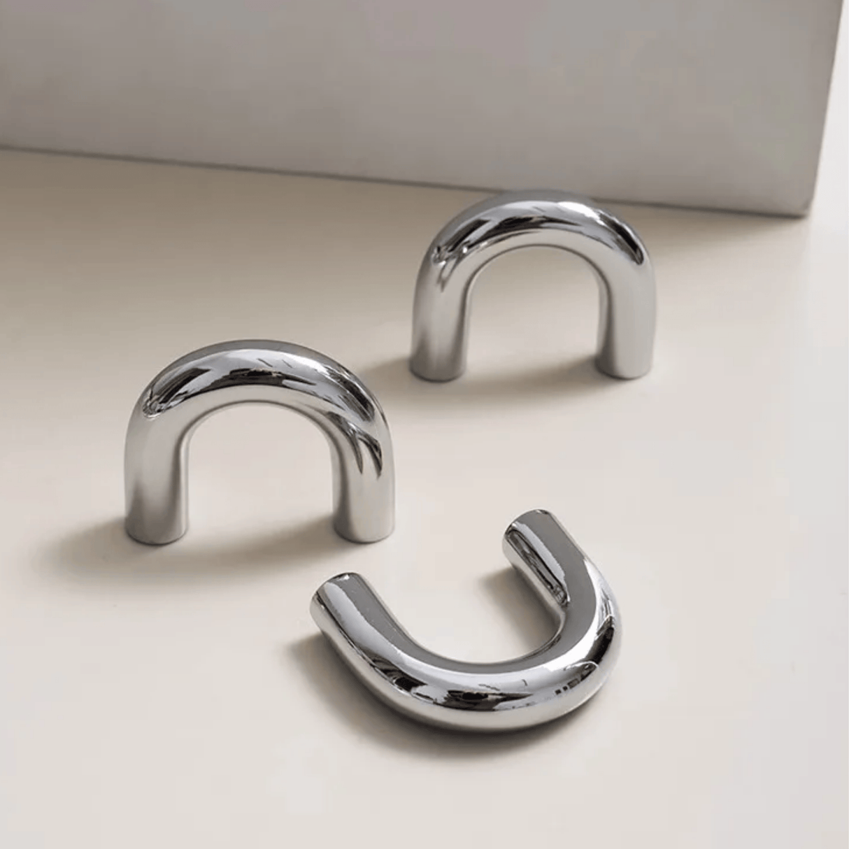 Three chrome U-shaped hooks on a light beige surface with a neutral background
