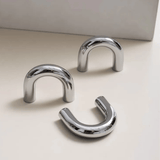 Three chrome U-shaped hooks on a light beige surface with a neutral background