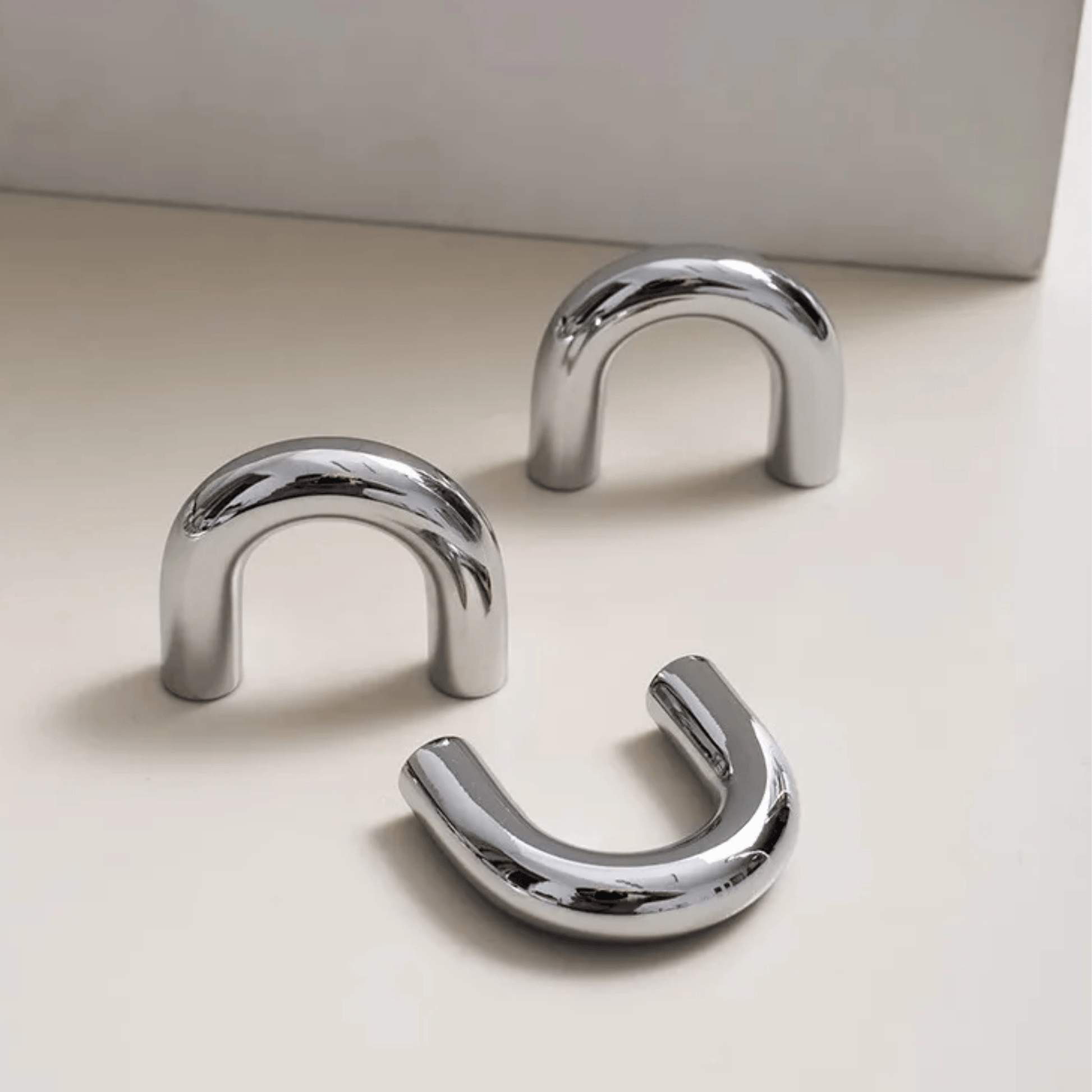 Three chrome U-shaped hooks on a light beige surface with a neutral background