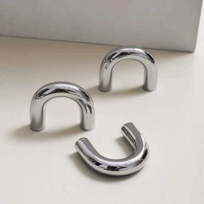 Three chrome U-shaped hooks on a light beige surface with a neutral background