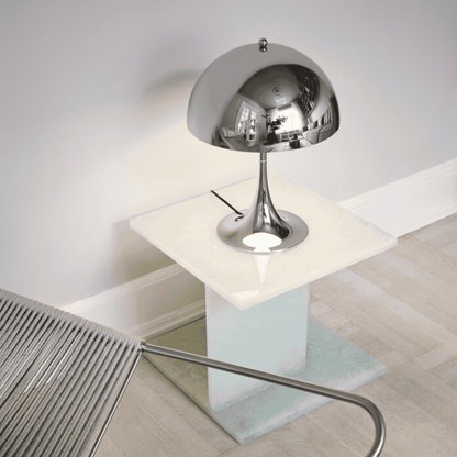 Modern silver table lamp on a glass table with a chair in the background