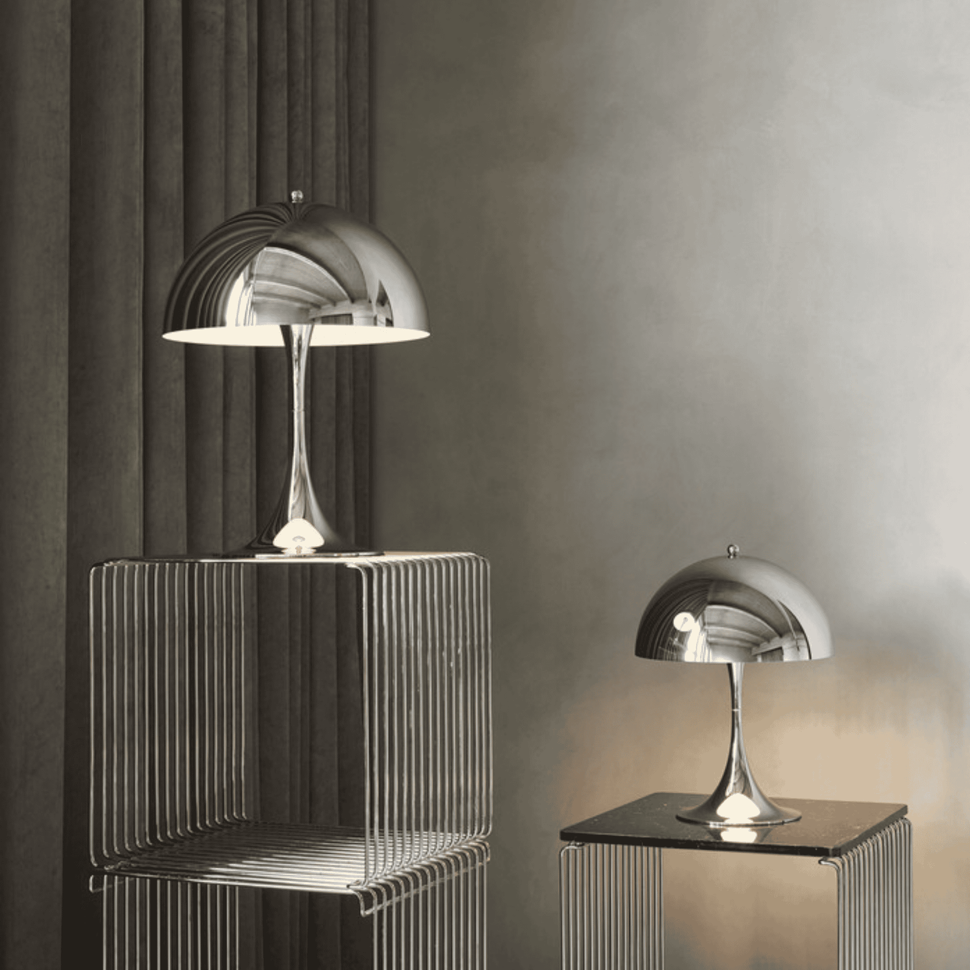 Two modern silver table lamps on decorative stands against a gray wall.