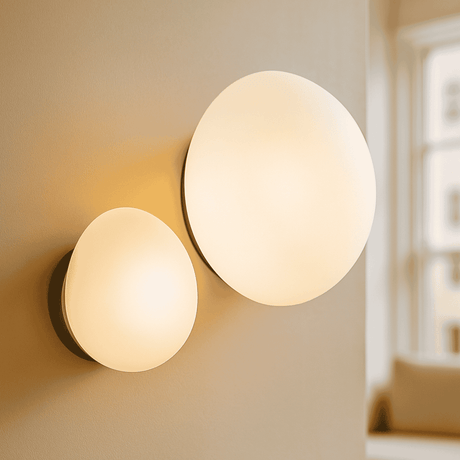 Two round wall lights on a beige wall with a blurred room background