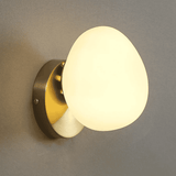 Wall-mounted light fixture with a round glass shade on a gray wall.