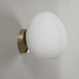 Wall-mounted light fixture with a white glass shade and brass finish on a gray wall.