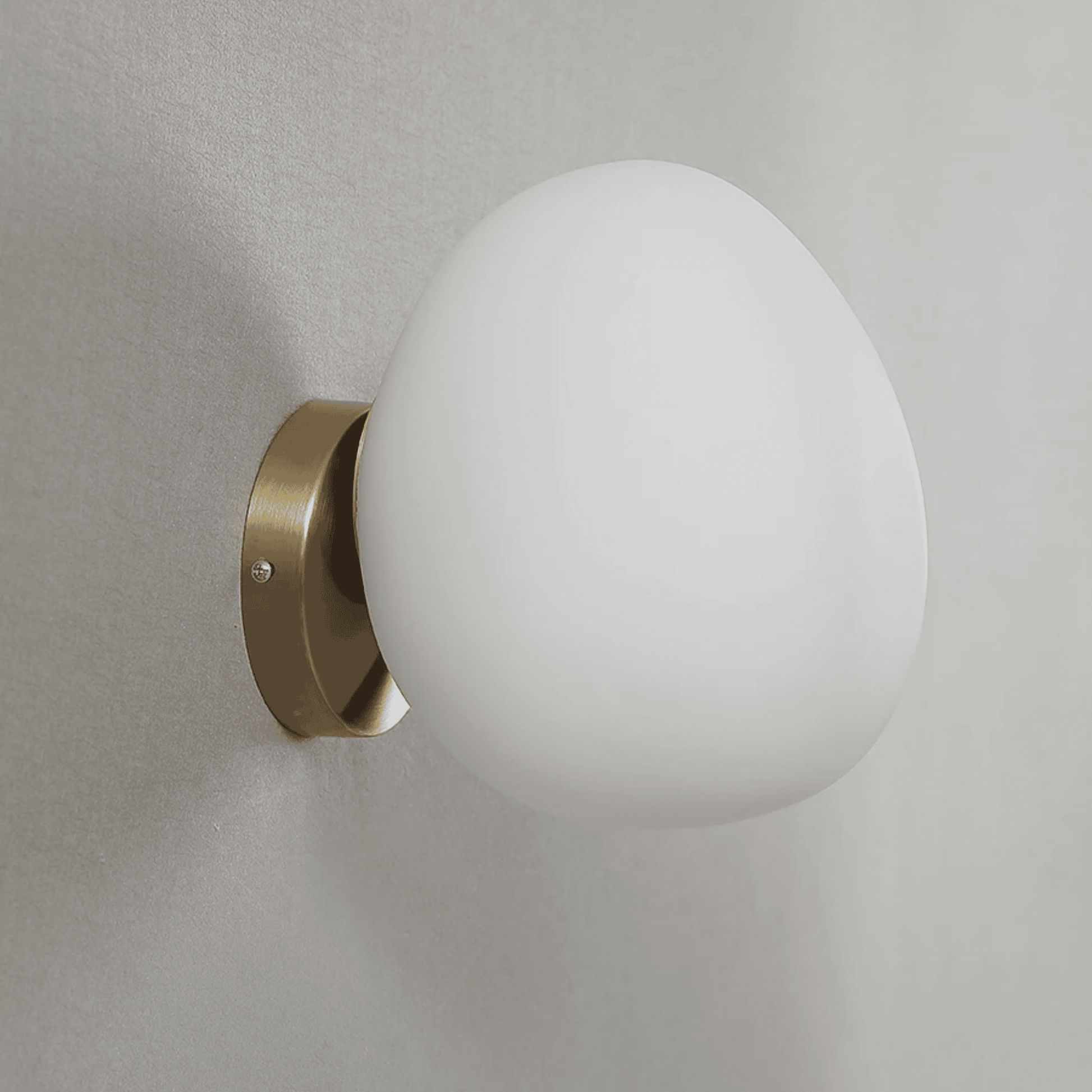Wall-mounted light fixture with a white glass shade and brass finish on a gray wall.