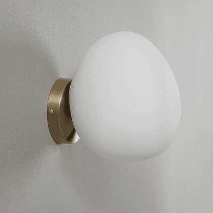 Wall-mounted light fixture with a white glass shade and brass finish on a gray wall.
