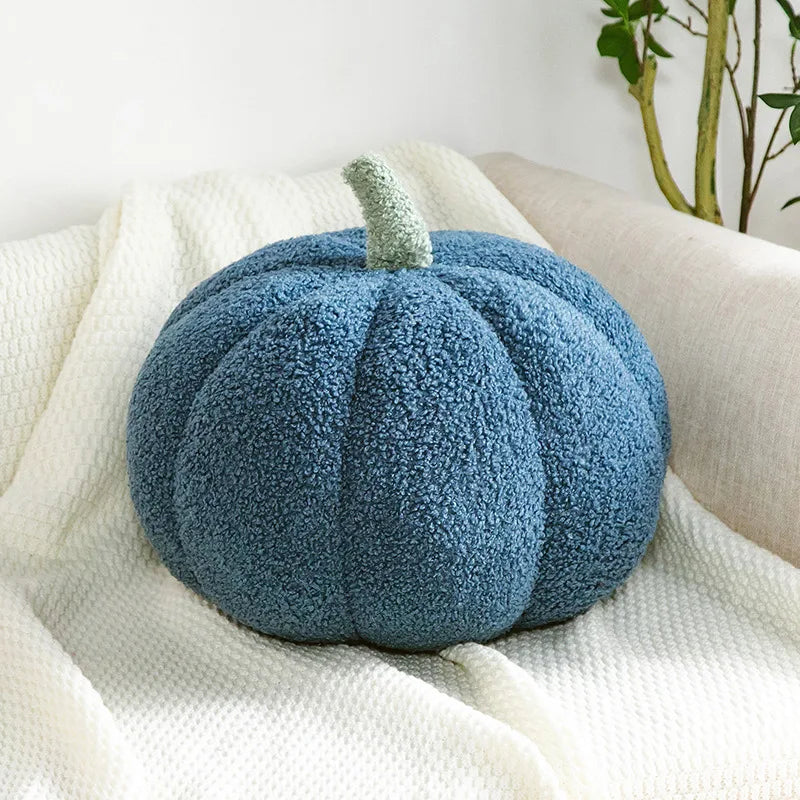 Blue textured pumpkin pillow on a white surface with a plant in the background