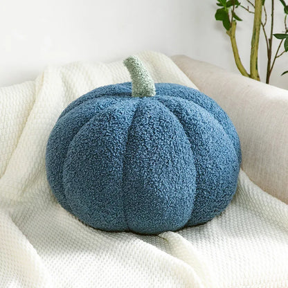 Blue textured pumpkin pillow on a white surface with a plant in the background