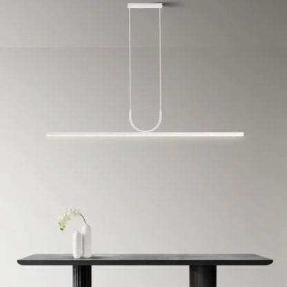 A sleek, modern pendant light hangs over a dark table with a white vase and orchid, creating a minimalist, elegant atmosphere.