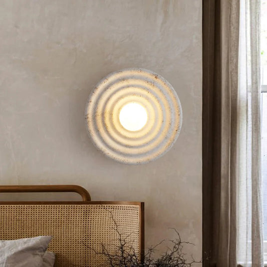 Round wall light fixture on a neutral wall with a bed and window in the background
