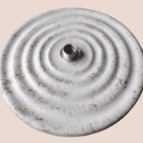 Round metallic object with concentric circles and a central hole on a beige background