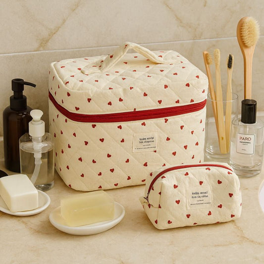 Beige toiletry bag with red heart pattern on a bathroom counter with toiletries.