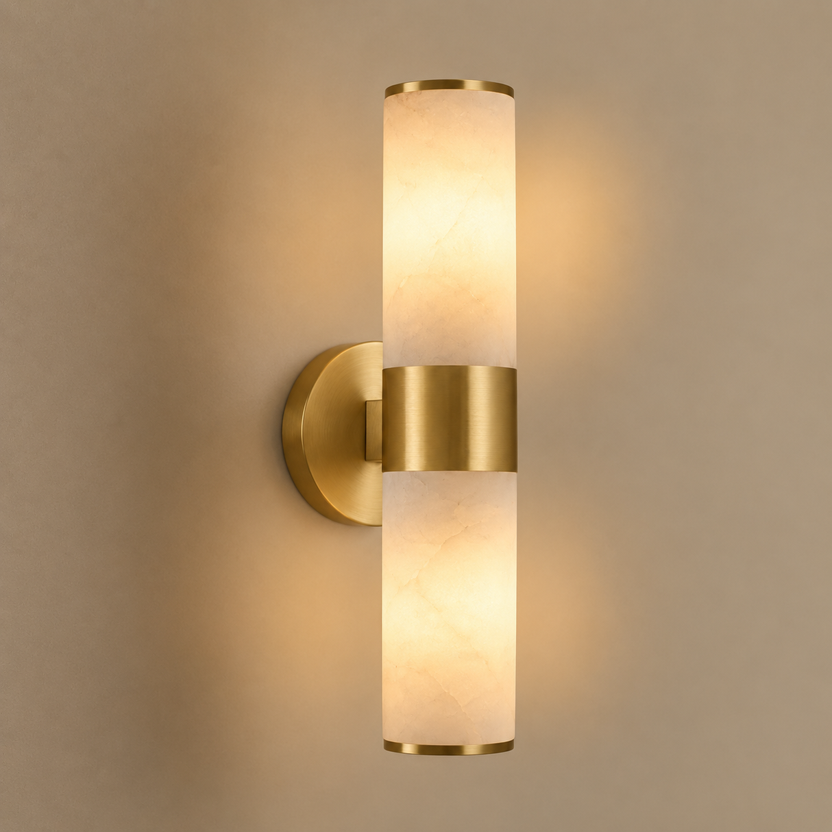 A modern cylindrical wall sconce light fixture with a brushed gold metal finish and a warm glowing cream-colored textured glass shade, mounted on a beige wall.
