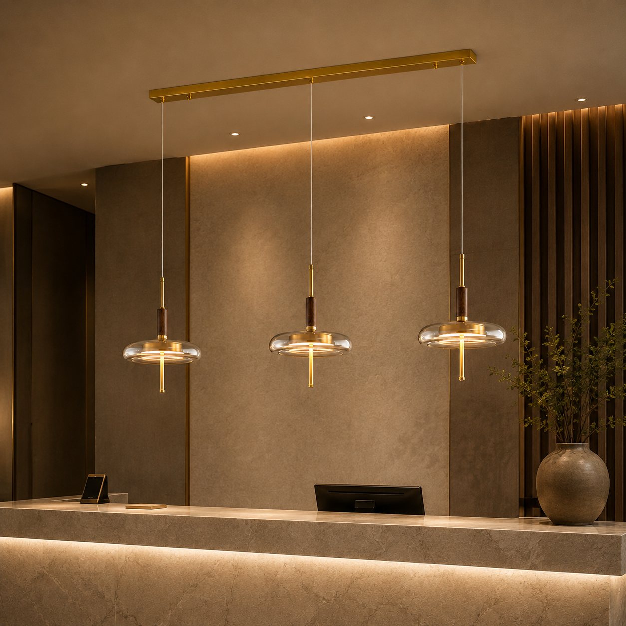 Three modern pendant lights with clear glass oval shades and brushed gold hardware hang over a reception desk in a warm, contemporary lobby setting.