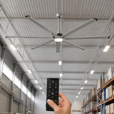 Ceiling fan in a warehouse setting with a hand holding a remote control.