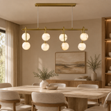 Marble ball light – L100cm Brass – lifestyle Installed above dining table in elegant warm beige dining room, ceiling connection visible, exact scale relative normal furniture.