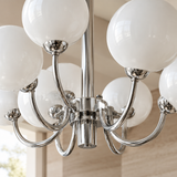 Chrome glass chandelier – 9 heads Chrome – close-up light off Tight lower side macro of chrome hub and curling arms joining white glass, lamps completely OFF, natural daylight only. Fixture partially outside frame.