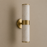A modern cylindrical wall sconce with a white marble-look glass shade and brushed gold metal accents, mounted on a warm beige wall.