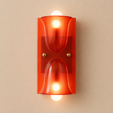 A modern wall-mounted light fixture with a translucent orange-red glass shade and two glowing warm white bulbs, centered against a plain beige wall.
