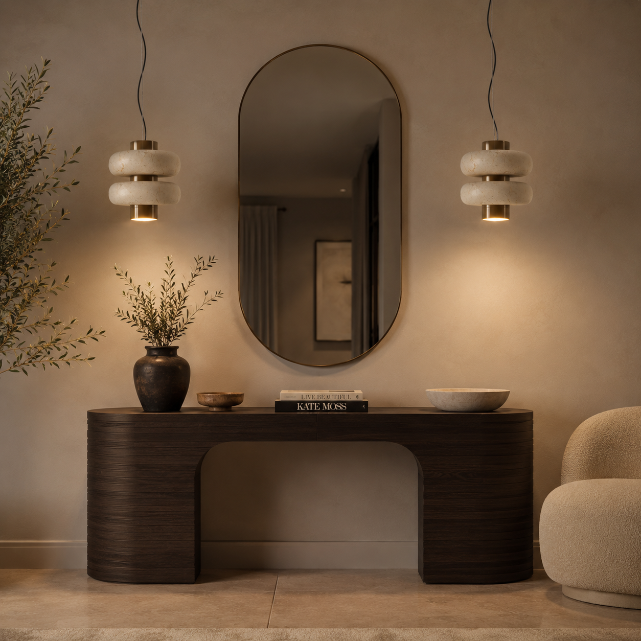 A modern dark wood console table in a warm, minimalist interior setting, styled with a dark ceramic vase, a small bowl, a book, and a white ceramic bowl. Above the table is a large, vertically-oriented oval mirror, flanked by two hanging pendant lights with white stacked glass shades and gold accents.