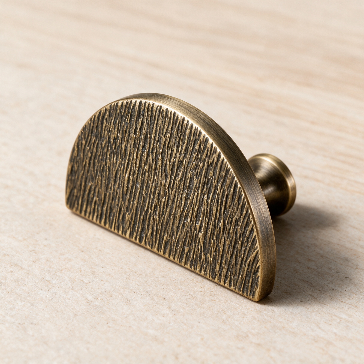 A vintage-style brass cabinet knob with a textured, brushed finish and a semi-circular half-moon shape, resting on a light wood surface.
