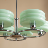 A close-up of a modern multi-light chandelier with glossy pale mint green glass shades and a polished silver metal frame, set against a solid warm beige background.