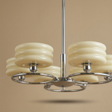 A modern multi-light chandelier with cream-colored stacked disc shades and polished chrome metal arms and central stem, shown against a solid warm beige background.