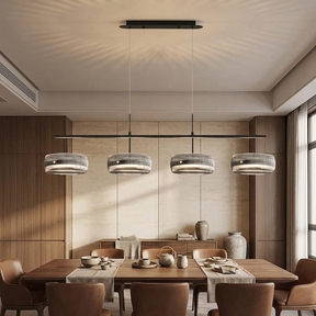 A modern 4-light linear ceiling pendant chandelier with textured gray and silver drum shades, suspended over a wooden dining table in a contemporary dining room.
