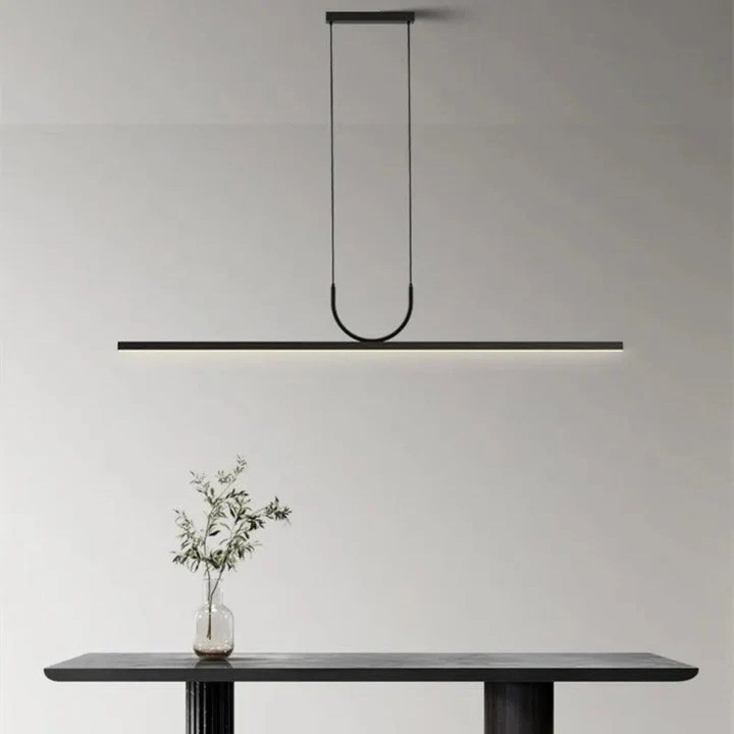 A black linear pendant light suspended above a simple dining table in a minimalist interior, highlighting the clean lines of the space.