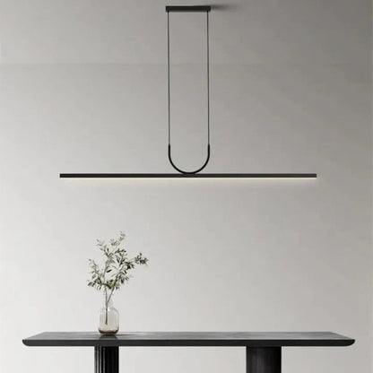 A black linear pendant light suspended above a simple dining table in a minimalist interior, highlighting the clean lines of the space.