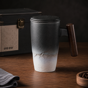 Kuro Artisan Ceramic Tea Infuser Mug in charcoal and white glaze with wooden handle on a warm timber table