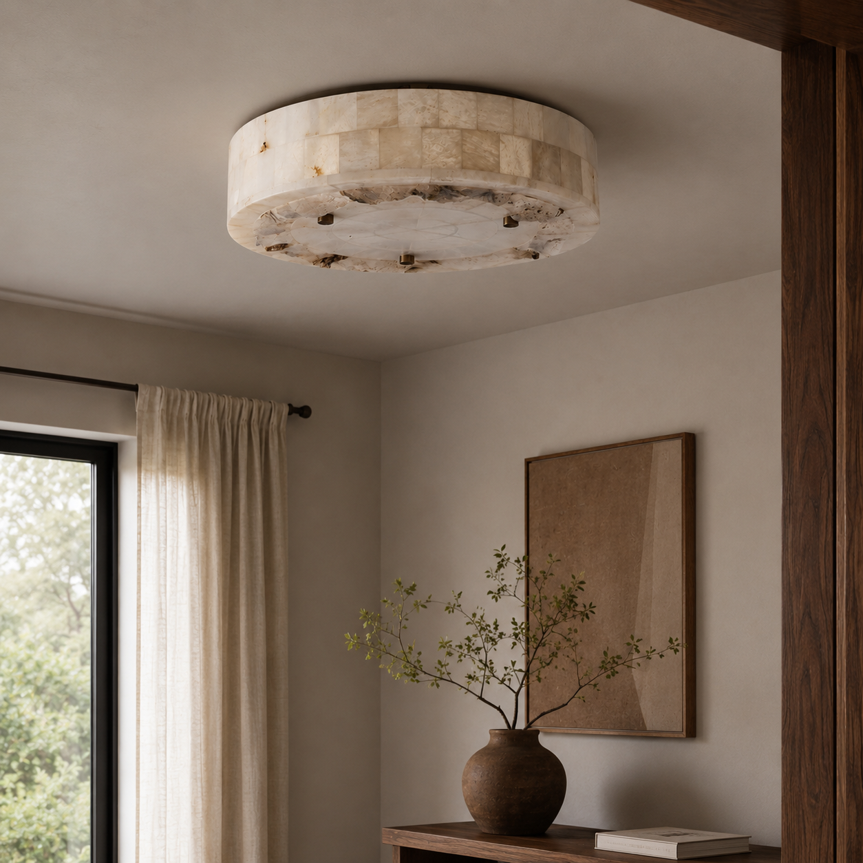 A round flush-mount ceiling light fixture made of natural beige stone with dark mineral inclusions, installed in a modern room with neutral walls, a window with curtains, and a wooden console table.