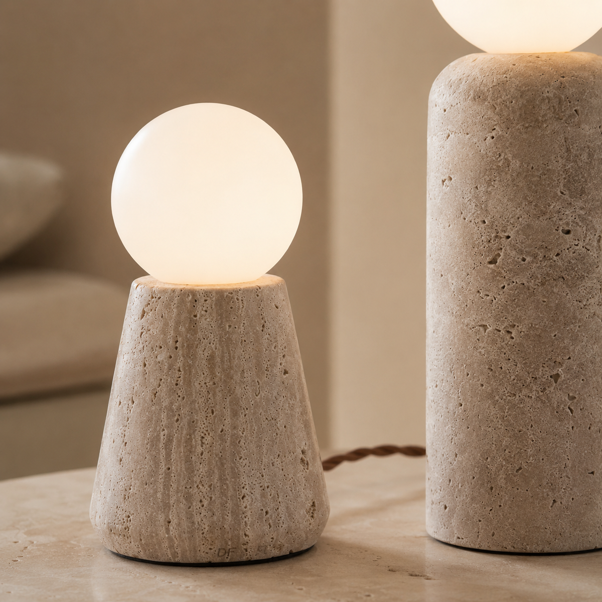 Two modern table lamps with textured stone bases and glowing frosted spherical shades, shown on a tabletop in a softly lit interior setting.