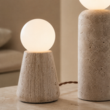 Two modern table lamps with textured stone bases and glowing frosted spherical shades, shown on a tabletop in a softly lit interior setting.