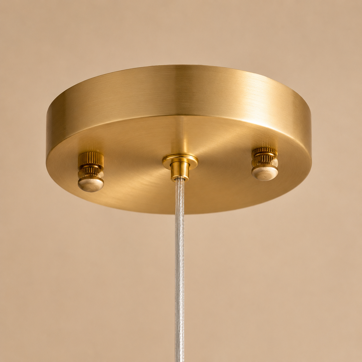 A close-up of a brushed brass ceiling canopy with two light sockets and a white cord hanging down against a warm beige background.