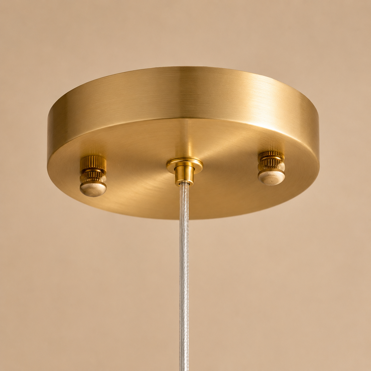 A close-up of a brushed brass ceiling canopy with two light sockets and a white cord hanging down against a warm beige background.