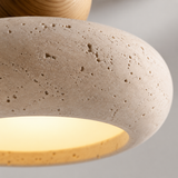 Close-up of a modern pendant light with a textured beige travertine stone shade and a warm yellow illuminated interior, with a wooden finial visible at the top.