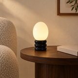 Black egg-shaped table lamp with glossy black stone base in a modern reading corner