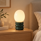 Green egg-shaped table lamp with dark green stone base in a warm modern bedroom